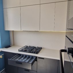 Meble & Tarasy - Nowoczesna kuchnia z czarnymi dolnymi szafkami i białymi górnymi, otwartą szufladą na sztućce, płytą gazową i marmurową podłogą.