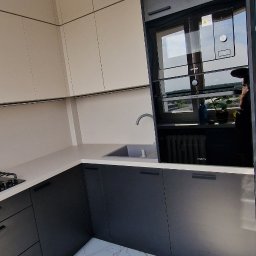 Meble & Tarasy - Nowoczesna kuchnia z szarymi szafkami dolnymi i beżowymi górnymi, biały blat, marmurowe płytki podłogowe i widoczne urządzenie AGD.
