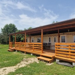 Meble & Tarasy - Domek letniskowy z drewnianym zadaszonym tarasem, widok z zewnątrz, w tle biały namiot ogrodowy.