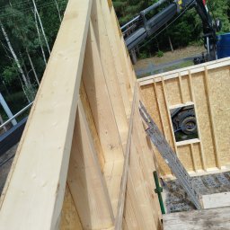 Viktor Kozachuk Uslugi OgulnoBudowlane - Konstrukcja drewniana ścian szkieletowych z widocznym oknem i dźwigiem w tle, etap budowy domu. Widok z góry na konstrukcję, z drabina opartą o ścianę.