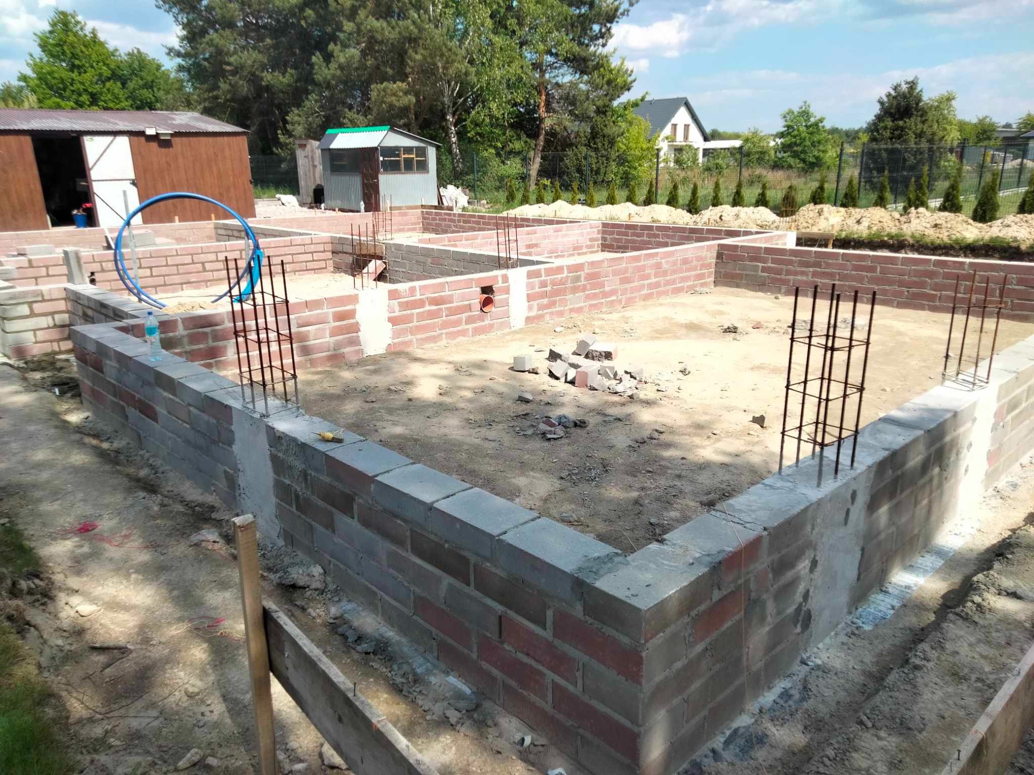 Murowane ściany fundamentowe zbrojone stalą, widok z góry na placu budowy w Żyrardowie. Częściowo zalane betonem, przygotowane do dalszych prac.