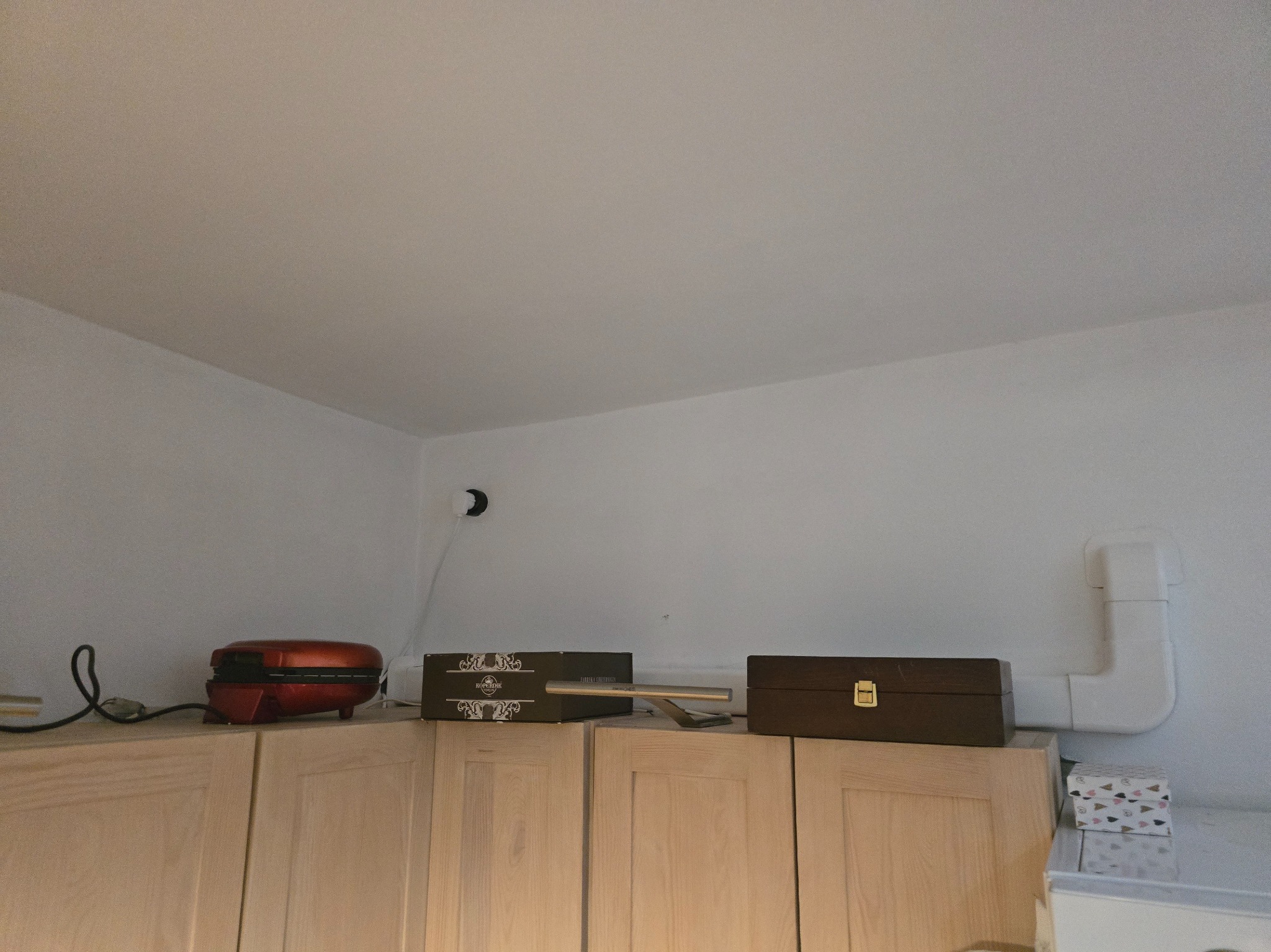 Biała rura wentylacyjna z kolankami, zamontowana tuż pod sufitem, obok szafek kuchennych z różnymi przedmiotami na nich.