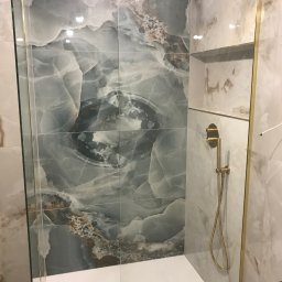 Bau best - Kabina prysznicowa z marmurowymi płytkami w odcieniach szarości i beżu, złota armatura, deszczownica i odpływ liniowy w białym brodziku.