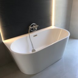 Bau best - Nowoczesna, wolnostojąca wanna w minimalistycznej łazience z czarną, teksturowaną ścianą i subtelnym oświetleniem LED, uzupełniona chromowaną armaturą i błyszczącymi płytkami podłogowymi.