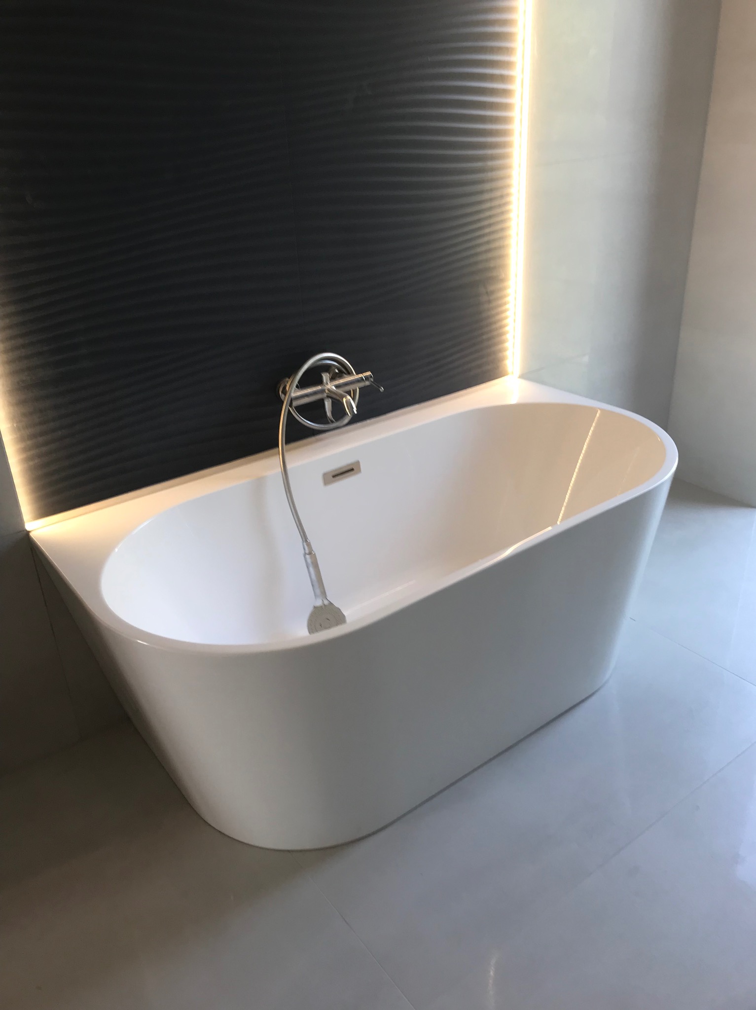 Nowoczesna, wolnostojąca wanna w minimalistycznej łazience z czarną, teksturowaną ścianą i subtelnym oświetleniem LED, uzupełniona chromowaną armaturą i błyszczącymi płytkami podłogowymi.