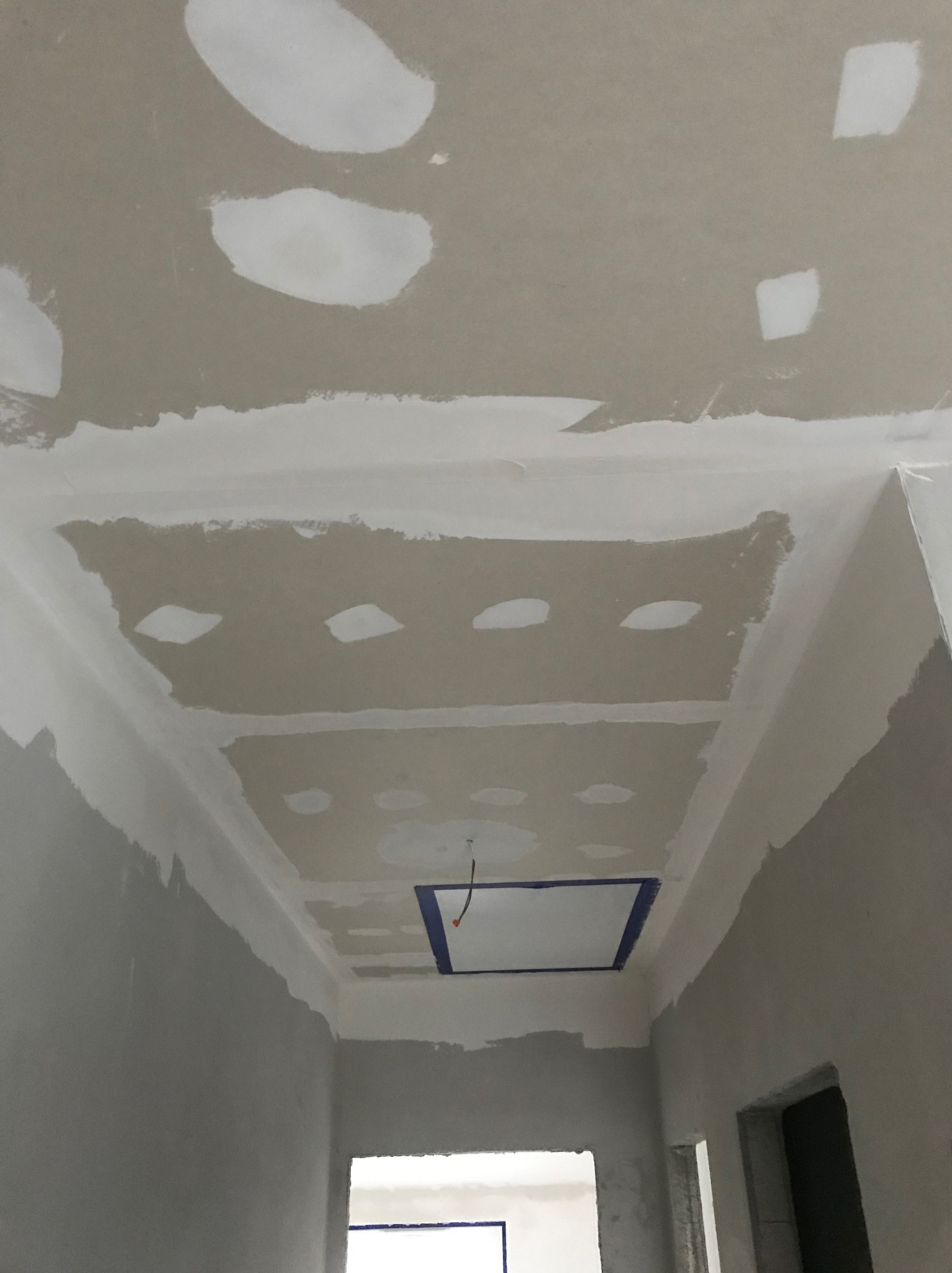 Sufit z płyt kartonowo-gipsowych w trakcie szpachlowania, widoczne łączenia płyt i otwór zabezpieczony taśmą malarską, surowy stan wykończenia.