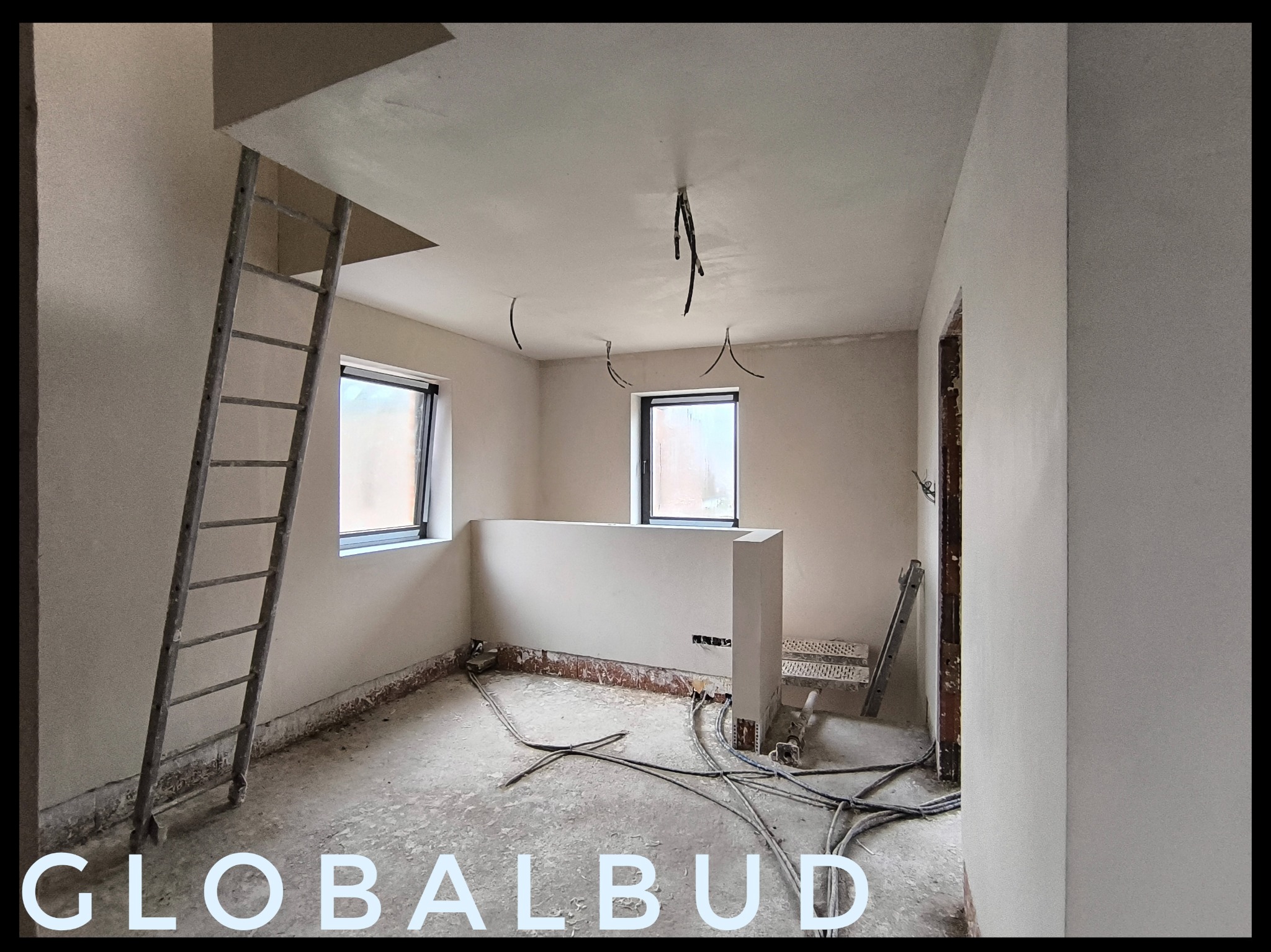 Pokój w trakcie prac wykończeniowych: świeżo otynkowane ściany, widoczne kable elektryczne, drabina oparta o ścianę, surowy beton na podłodze.