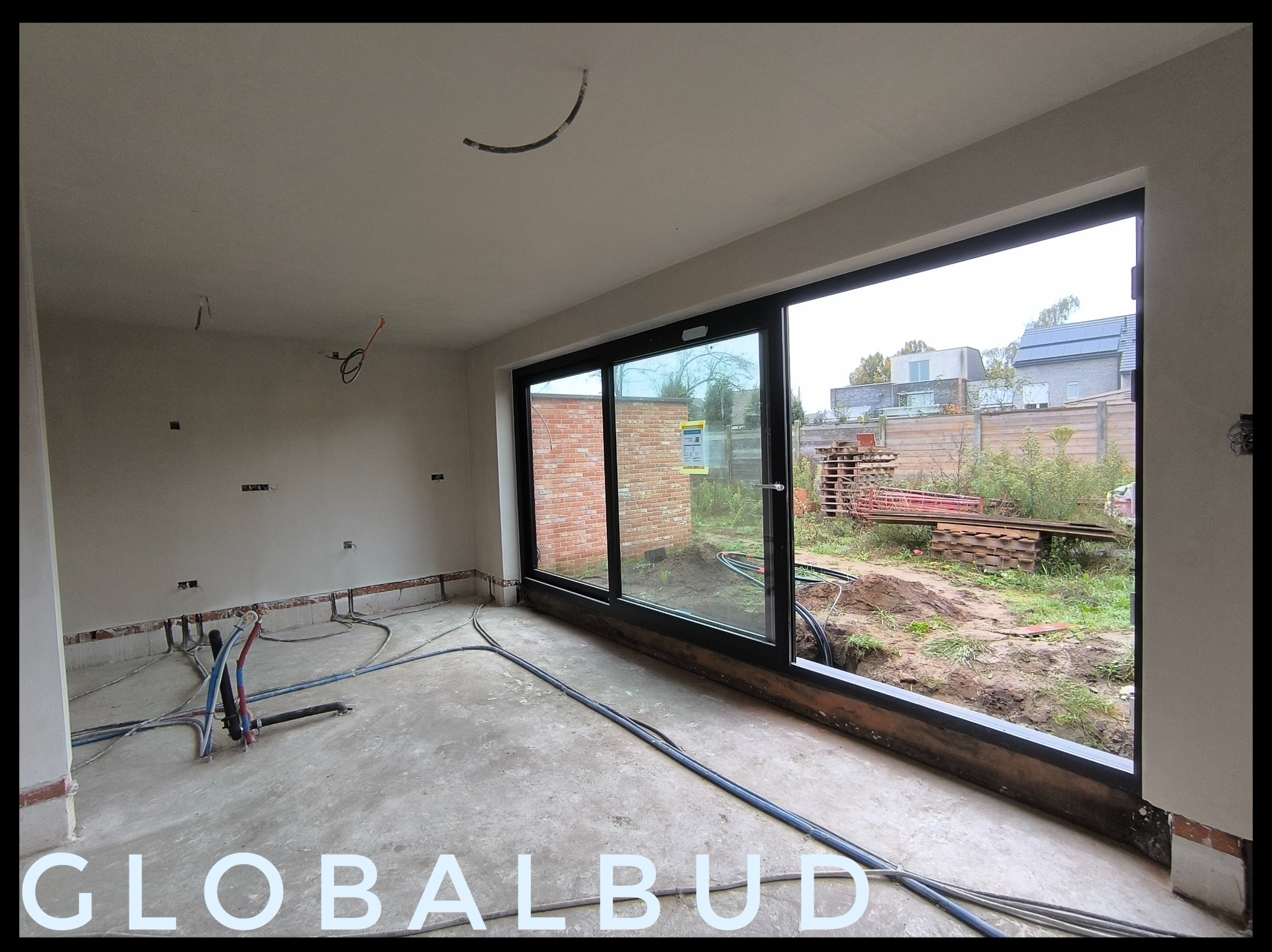 Wnętrze w stanie deweloperskim z dużym oknem przesuwnym, widoczne wystające kable i instalacje, ściany przygotowane pod wykończenie.