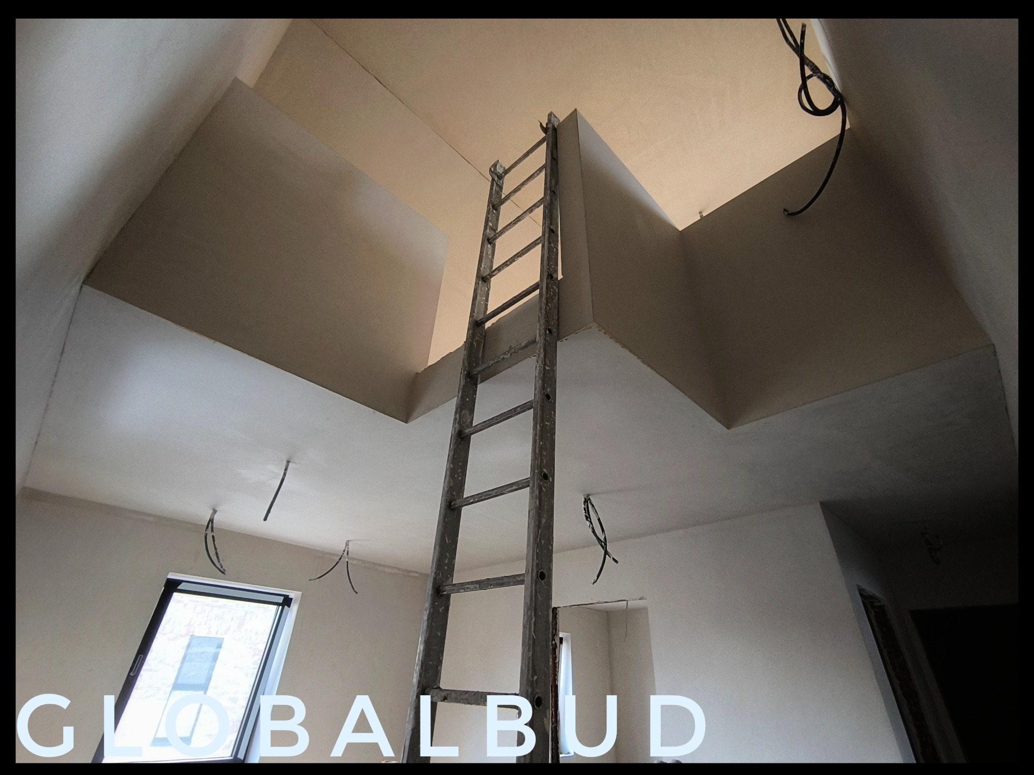 Wnętrze poddasza po wykonaniu gładzi gipsowej, widoczna drabina oparta o ścianę, okno dachowe i wystające przewody elektryczne.