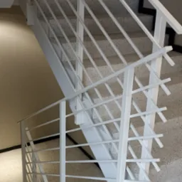 Białe, metalowe schody z minimalistyczną balustradą wewnątrz budynku, widok z góry na dół, schody wykończone lastryko.