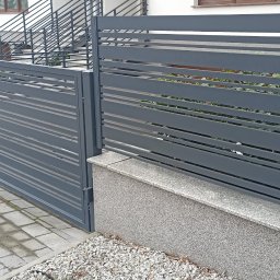 DAW-TECH - Nowoczesne, poziome, szare przęsła ogrodzeniowe z widocznymi elementami konstrukcyjnymi i słupkami z szarego kamienia, oddzielające posesję od chodnika z kostki brukowej.