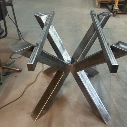 MARIUSZ GONDEK MAR-MONT - Surowa, spawana podstawa stołu z profili stalowych o geometrycznym kształcie gwiazdy, widoczne ślady spawania, w tle warsztat.