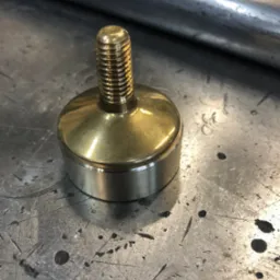 Mosiężny element tokarski z gwintem na metalowym stole warsztatowym z widocznymi śladami obróbki.