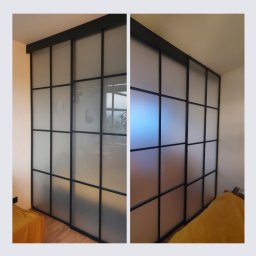 MARIUSZ GONDEK MAR-MONT - Przesuwne drzwi z czarnymi profilami i matowym szkłem tworzące podział przestrzeni w pokoju, widoczne elementy wyposażenia wnętrza.