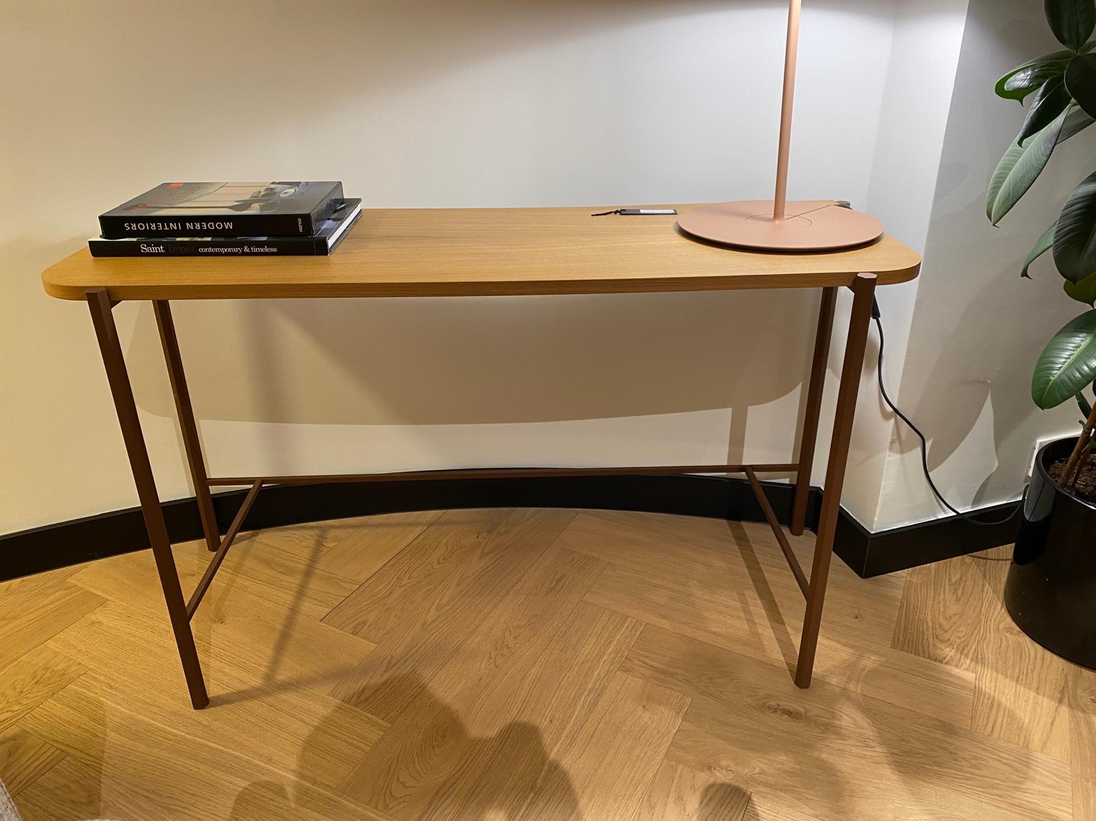 Biurko z drewnianym blatem i metalowymi nogami, oświetlone lampą stojącą, uzupełnione o książki, w minimalistycznym wnętrzu w Nadarzynie.