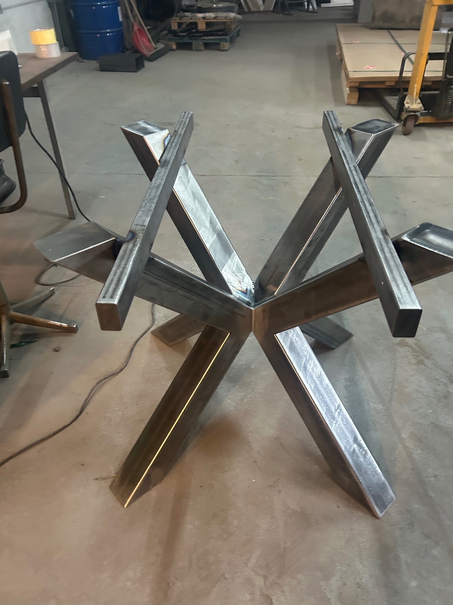 Surowa, spawana podstawa stołu z profili stalowych o geometrycznym kształcie gwiazdy, widoczne ślady spawania, w tle warsztat.