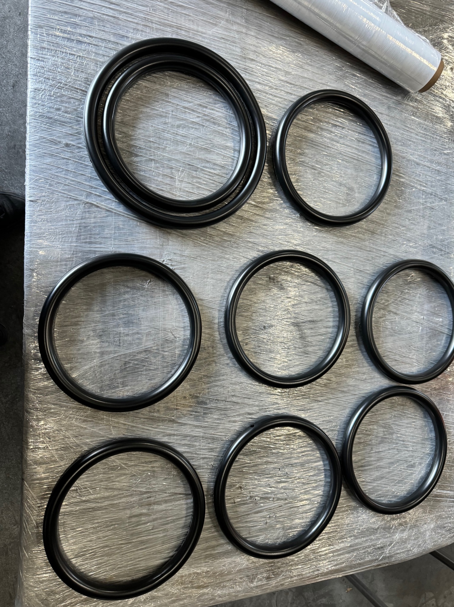 Zestaw czarnych, metalowych pierścieni o różnych średnicach, ułożonych na folii stretch na metalowym stole.