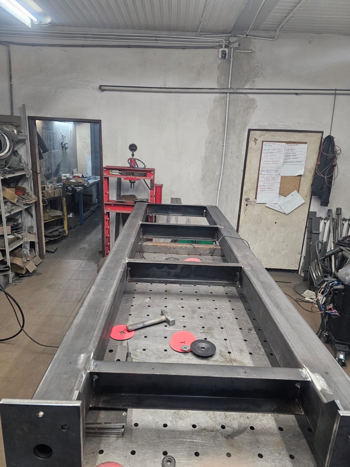 Metalowa rama konstrukcyjna w trakcie budowy, widoczna na stole spawalniczym z narzędziami, warsztat w tle.