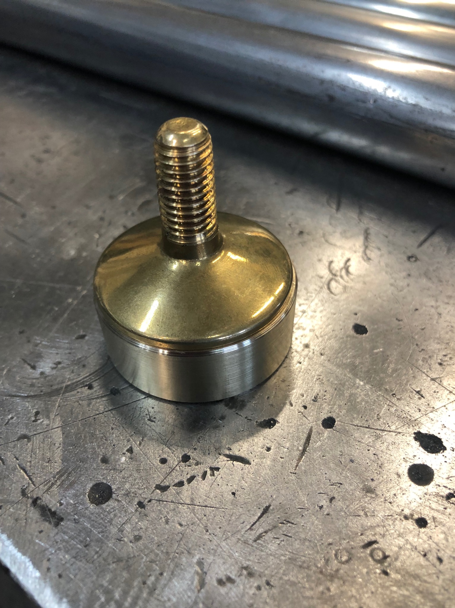 Mosiężny element tokarski z gwintem na metalowym stole warsztatowym z widocznymi śladami obróbki.