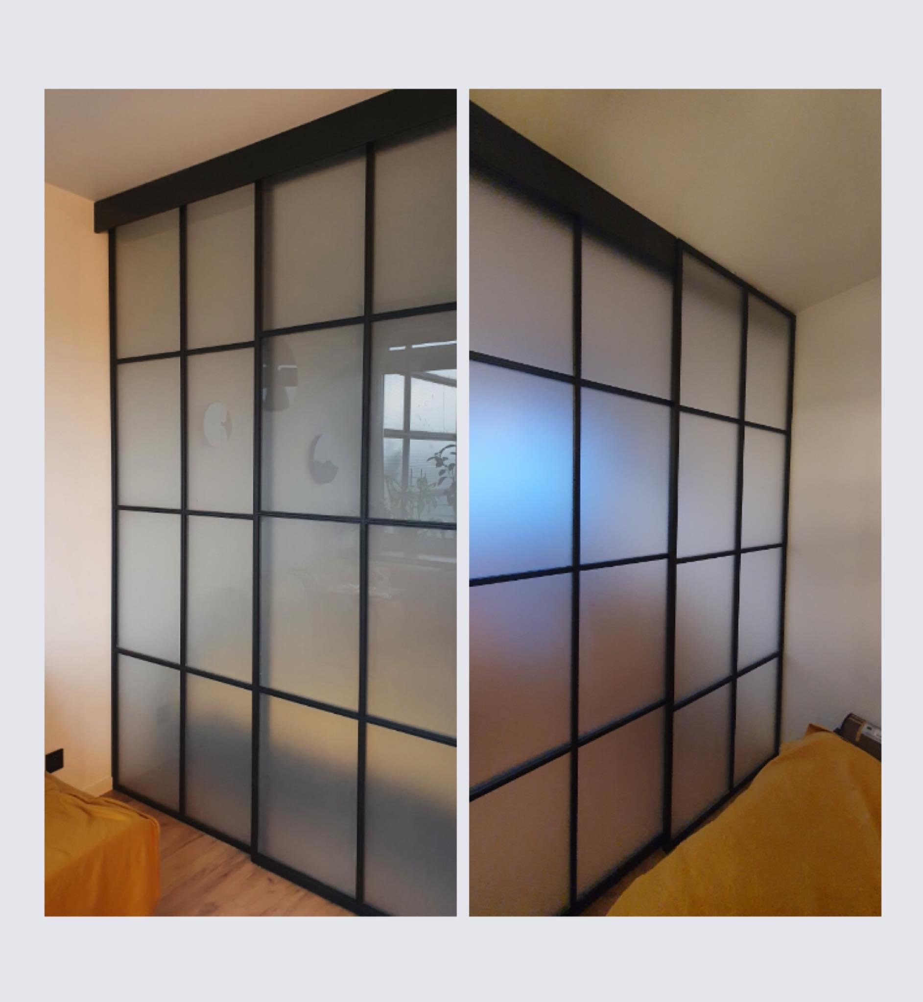 Przesuwne drzwi z czarnymi profilami i matowym szkłem tworzące podział przestrzeni w pokoju, widoczne elementy wyposażenia wnętrza.