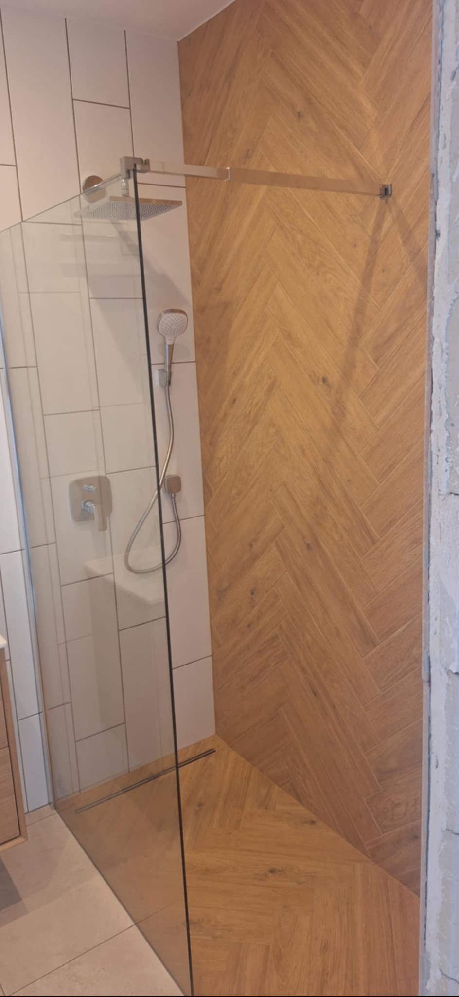 Nowoczesna kabina prysznicowa walk-in z drewnopodobną okładziną w jodełkę na ścianie i podłodze, chromowana armatura, białe płytki na sąsiedniej ścianie.