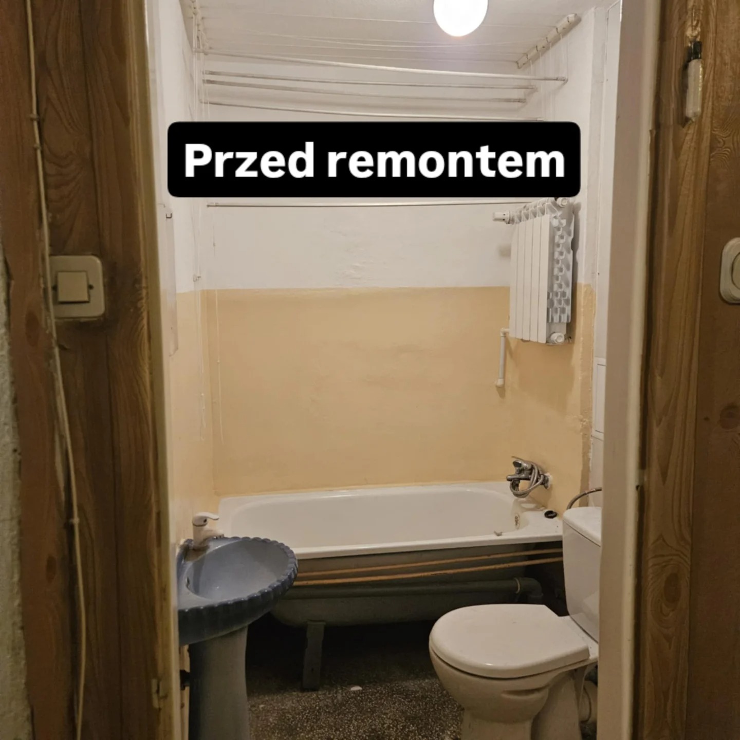 Łazienka z lat 90. przed remontem: stara wanna, umywalka na postumencie, sedes kompaktowy, żółte ściany, widok przez drewniane drzwi. Stan początkowy.