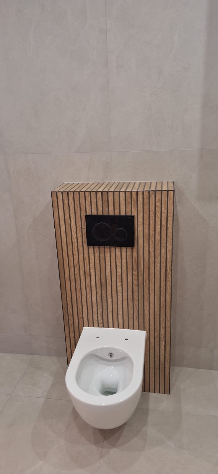 Wisząca toaleta z drewnianą obudową i czarnym panelem sterującym na tle płytek w odcieniach szarości. Nowoczesny design łazienki po remoncie.