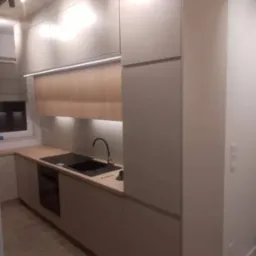 Nowoczesna kuchnia z jasnymi, drewnopodobnymi frontami, podświetleniem LED pod szafkami górnymi i czarnym zlewem z baterią, widok z boku na zabudowę sięgającą sufitu.