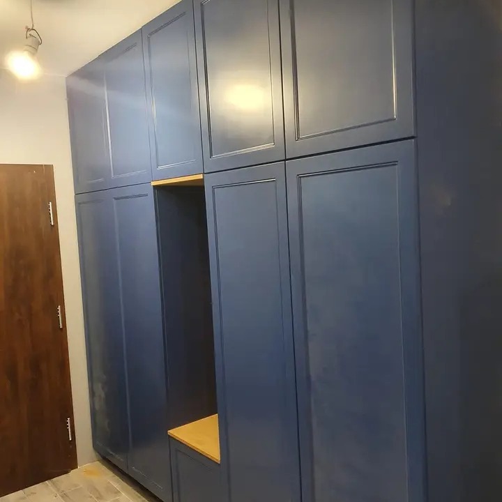 Wysoka, zabudowana szafa wnękowa w odcieniach granatu z drewnianym siedziskiem w otwartej wnęce.