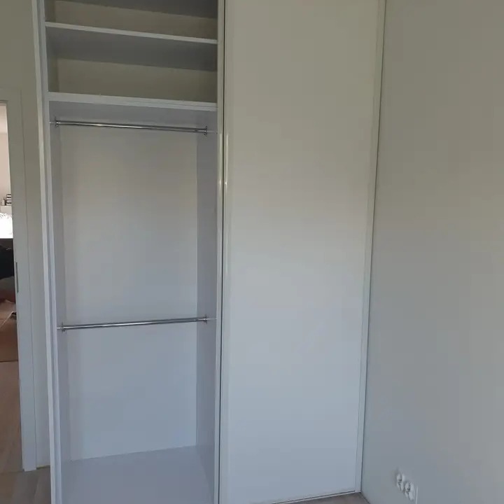 Biała szafa wnękowa z przesuwnymi drzwiami, widoczne wnętrze z półkami i drążkami na ubrania.