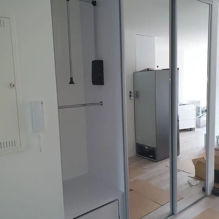 Wnętrze szafy wnękowej z przesuwnymi lustrzanymi drzwiami, widoczne elementy montażowe i częściowo wyposażone wnętrze, w tle pomieszczenie w trakcie remontu.