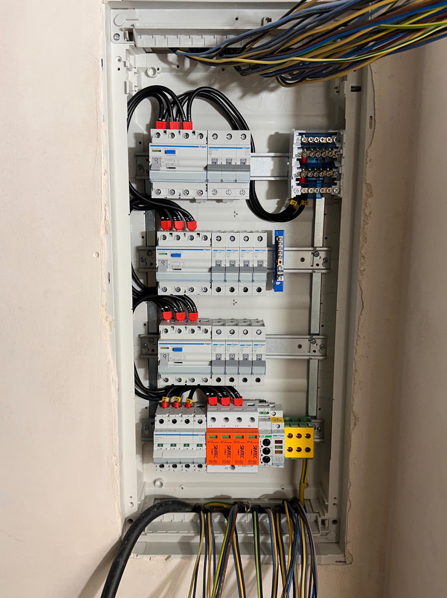 Rozdzielnica elektryczna w obudowie, widoczne zabezpieczenia nadprądowe Hager, ograniczniki przepięć Simtec, listwy zaciskowe, przewody w kolorach brązowym, niebieskim, żółto-zielonym i czarnym.