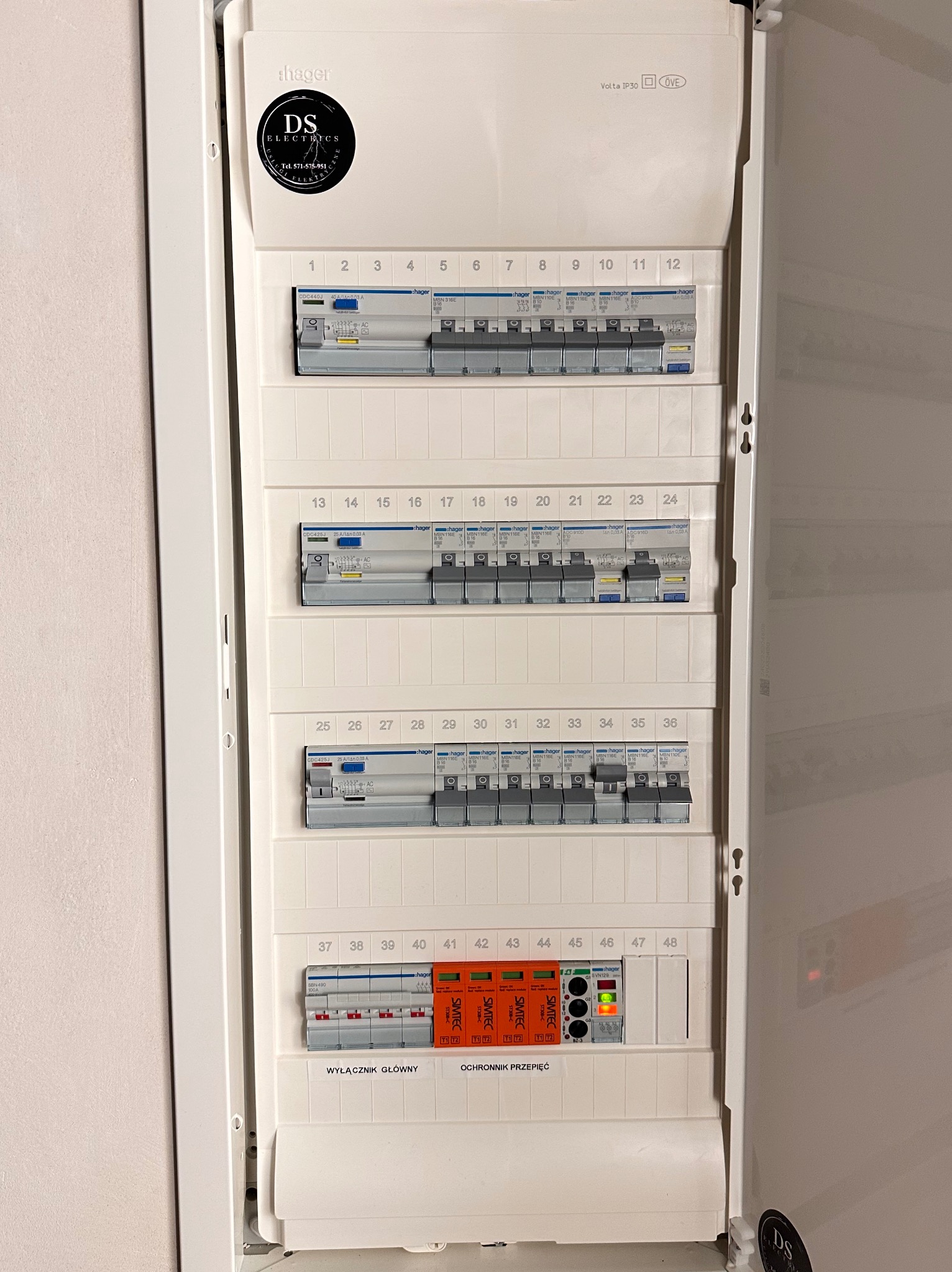 Otwarta skrzynka elektryczna Hager Volta IP30 z zamontowanymi bezpiecznikami, wyłącznikiem głównym i ochronnikiem przepięć Simtec ST308-C, oklejona naklejką z logo firmy DS Electrics.