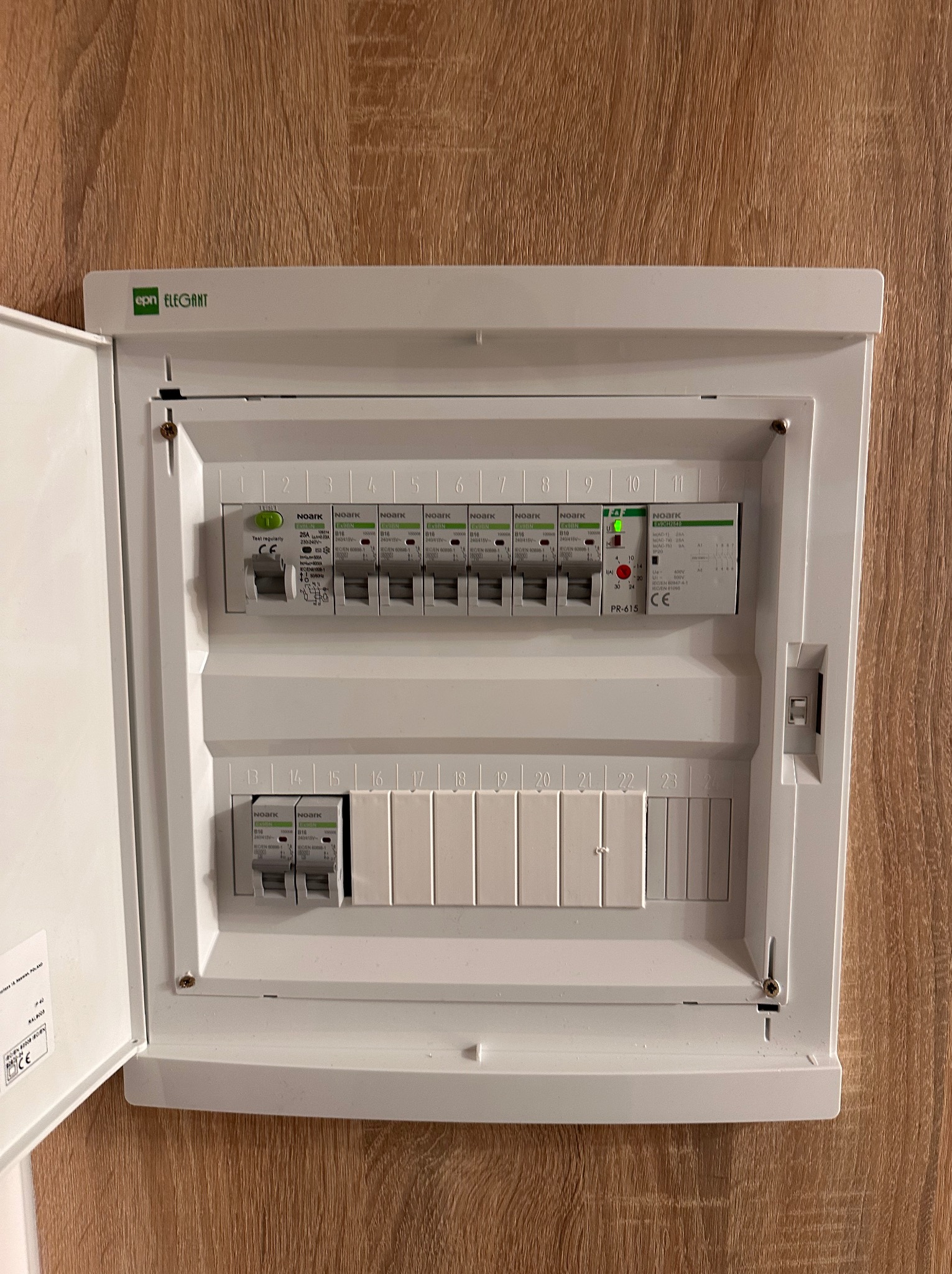 Otwarta skrzynka elektryczna z zainstalowanymi bezpiecznikami Noark na drewnianym tle, widoczne oznaczenia i parametry techniczne.