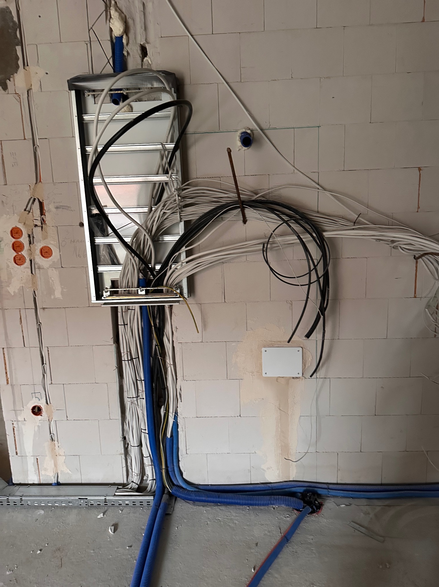 Rozprowadzenie przewodów elektrycznych w ścianie z betonu komórkowego, widoczne kable w peszlach i puszki instalacyjne. Etap prac przed tynkowaniem.