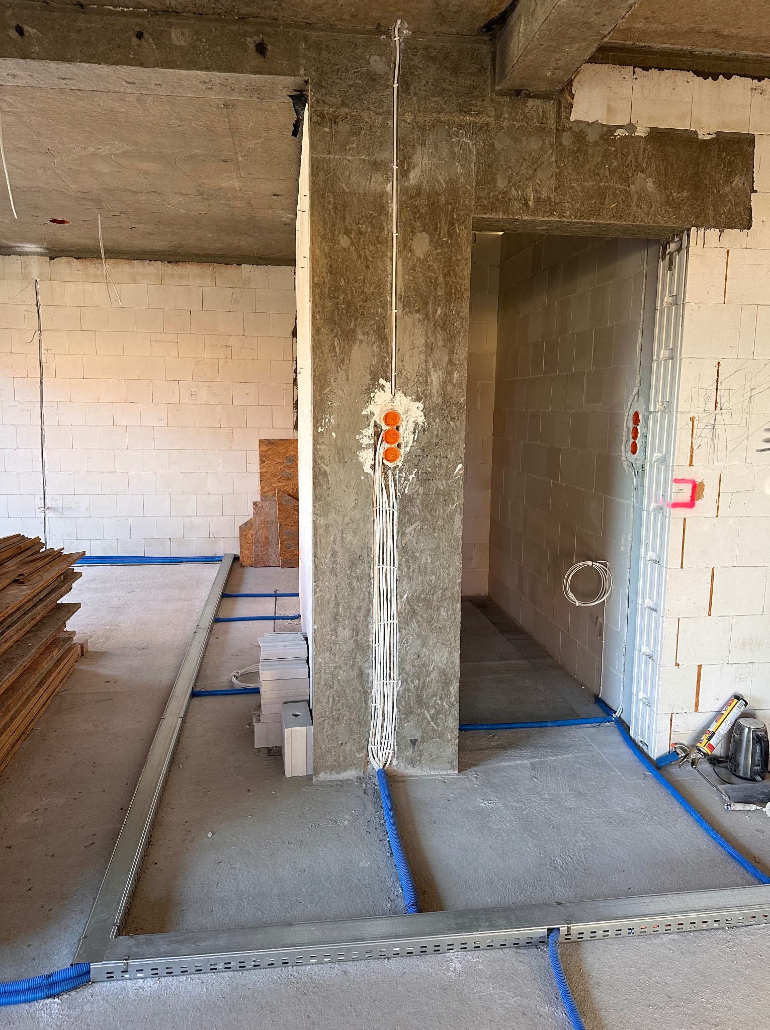 Surowy stan: kable w peszlach prowadzone wzdłuż ścian i podłogi wewnątrz budynku w trakcie budowy. Widoczne puszki instalacyjne i przewody.