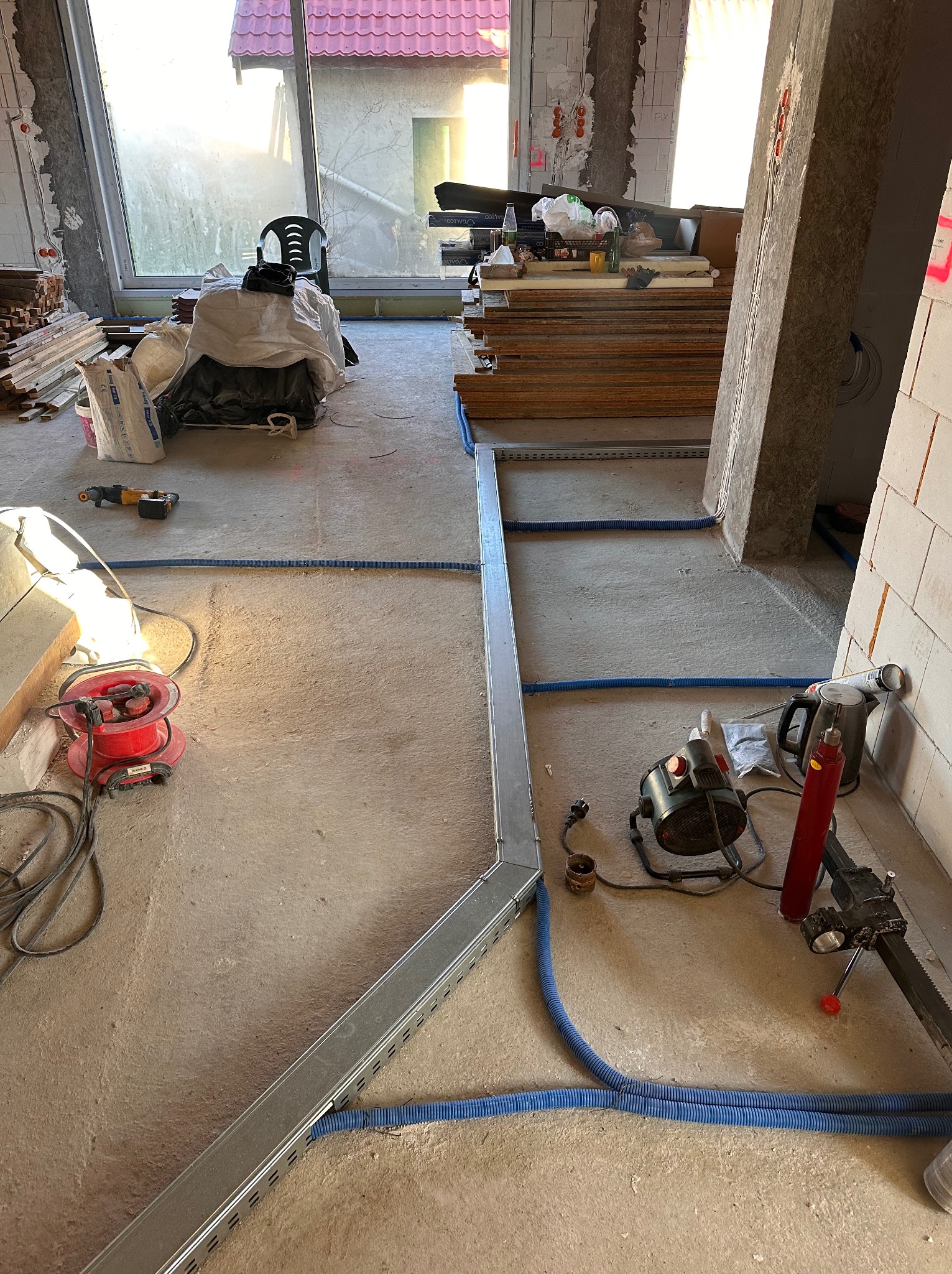 Wnętrze w trakcie prac instalacyjnych: widoczne koryto kablowe, niebieskie rury karbowane, narzędzia i materiały budowlane. Surowy stan wykończenia.