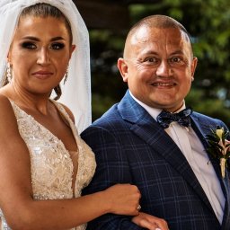 Karol Wierciński - Para młoda: uśmiechnięta panna młoda w bogato zdobionej sukni i welonie, oraz pan młody w granatowym garniturze w kratę z muszką, pozują do portretu w plenerze.