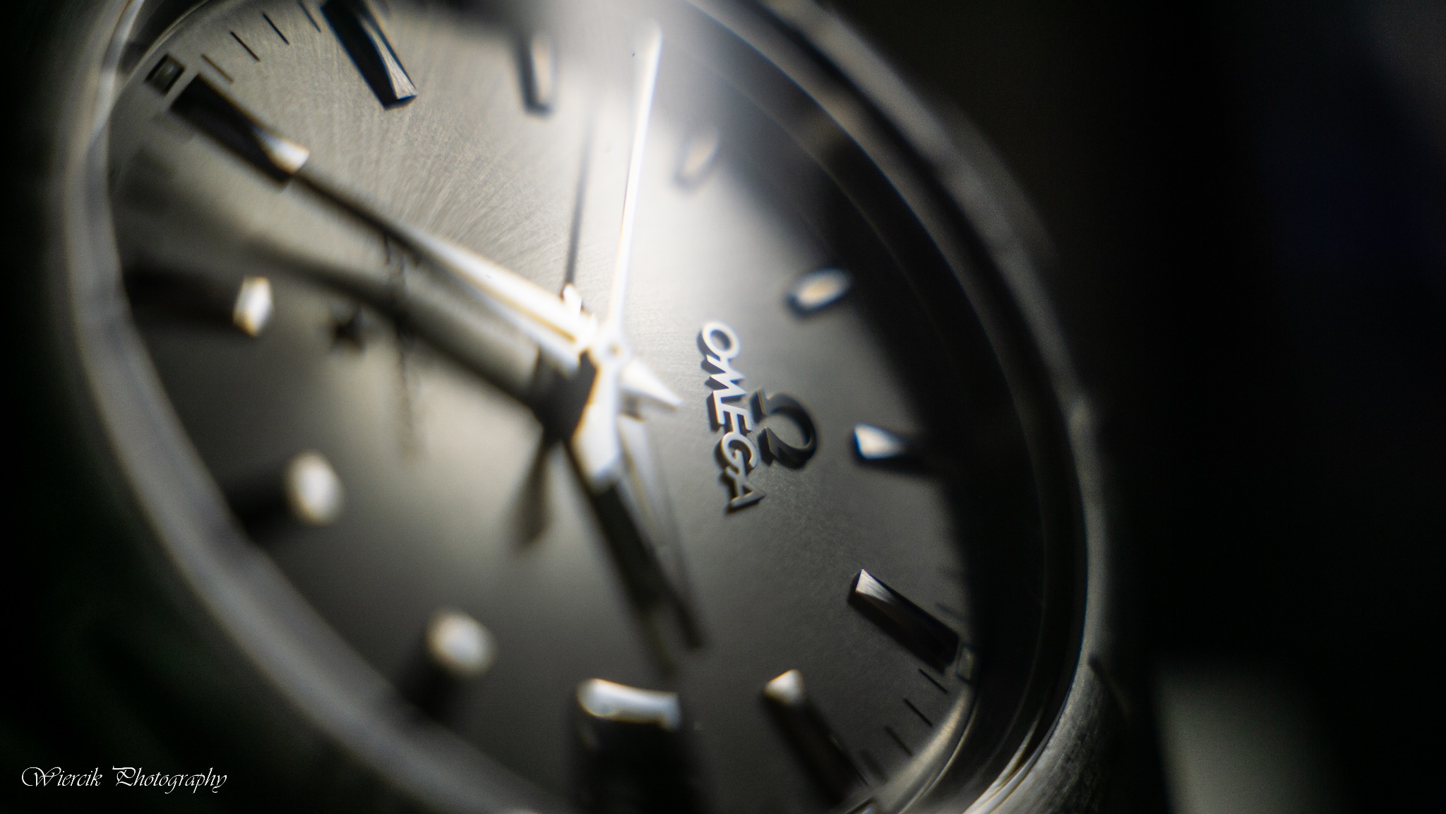 Zbliżenie na tarczę zegarka Omega z widocznymi wskazówkami i logo w ciemnej tonacji.