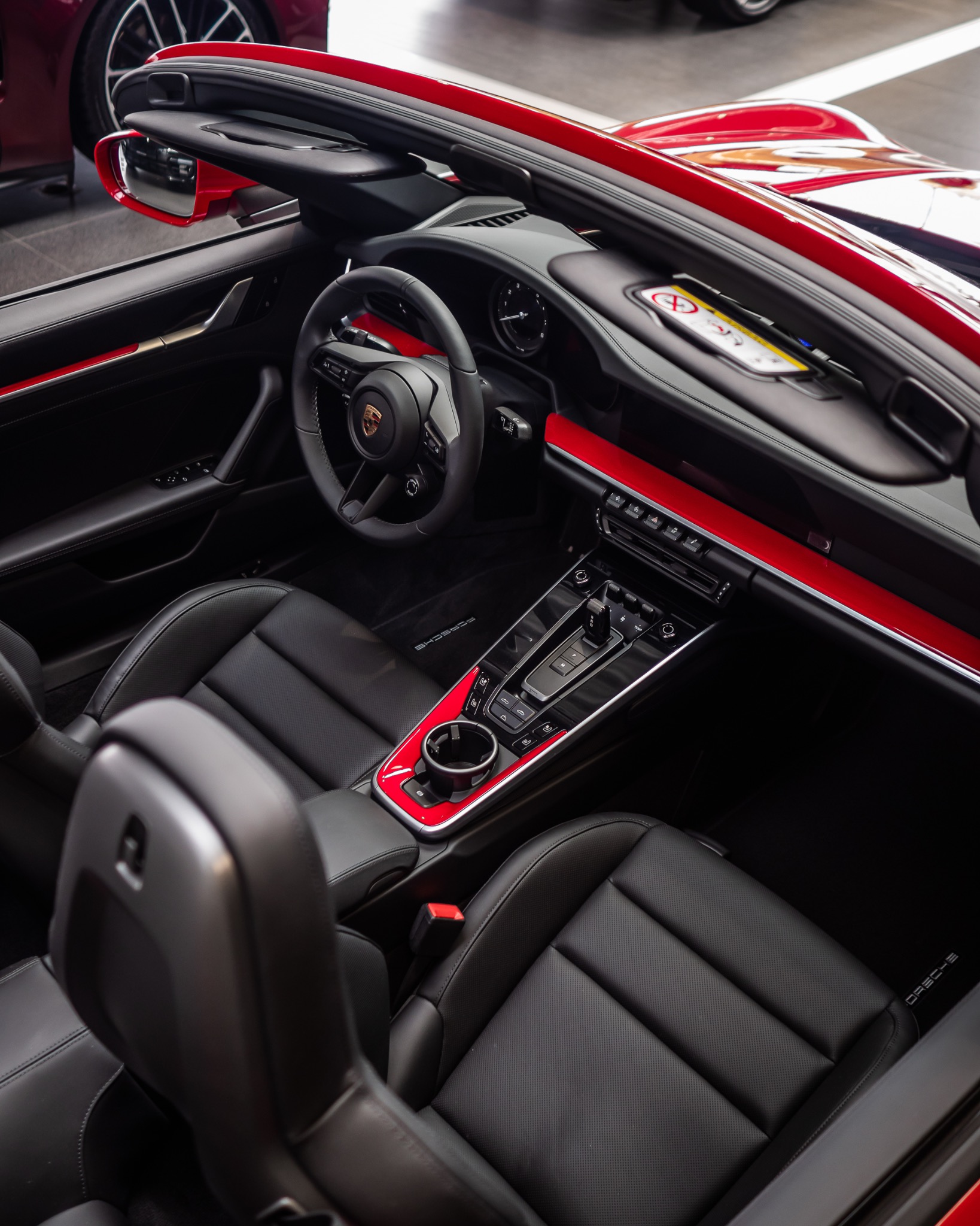 Wnętrze czerwonego Porsche 911 Cabriolet z czarną skórzaną tapicerką, widok z góry na deskę rozdzielczą, kierownicę z logo i fotele.