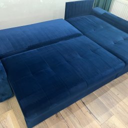 Mateusz Żylski - Rozłożona, granatowa kanapa z weluru na drewnianej podłodze, widoczne ślady po czyszczeniu na siedzisku.