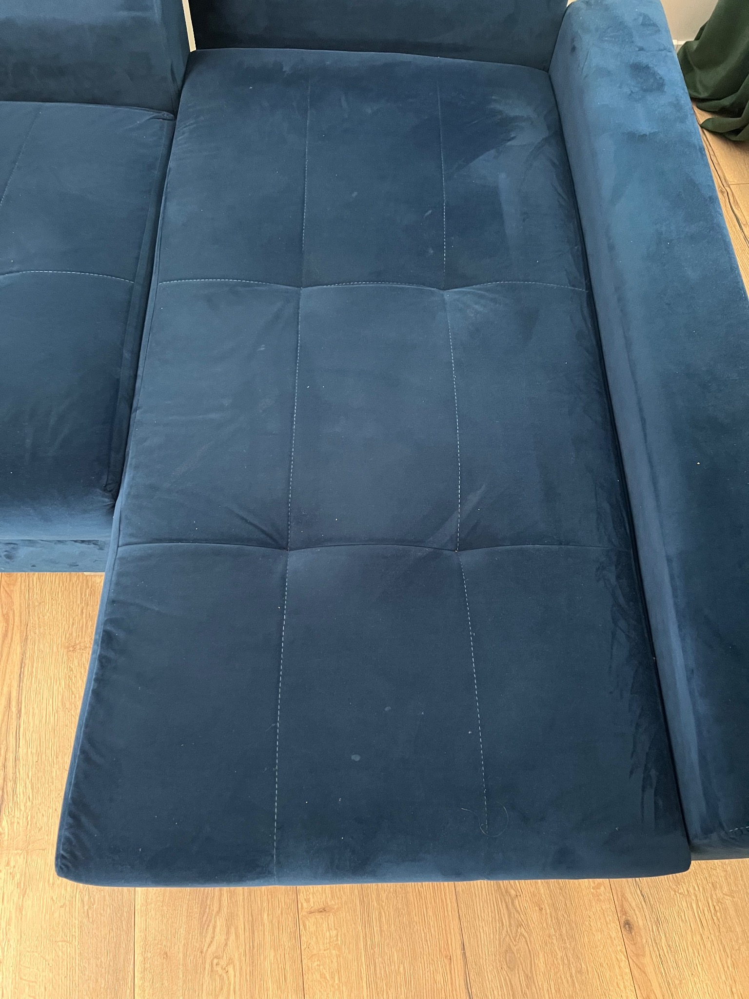 Fragment rozłożonej, ciemnoniebieskiej, welurowej sofy z widocznymi śladami czyszczenia na powierzchni, kwadratowe przeszycia, drewniana podłoga w tle.