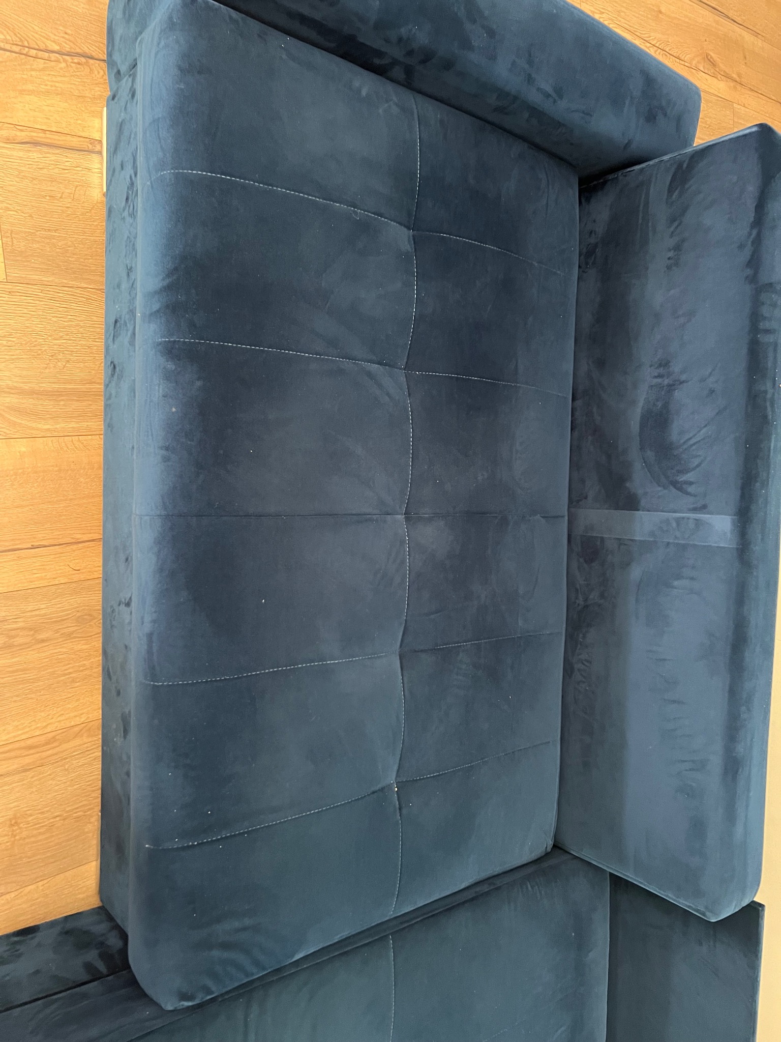 Granatowa, welurowa kanapa modułowa z pikowaniem, widoczna z góry na drewnianej podłodze.