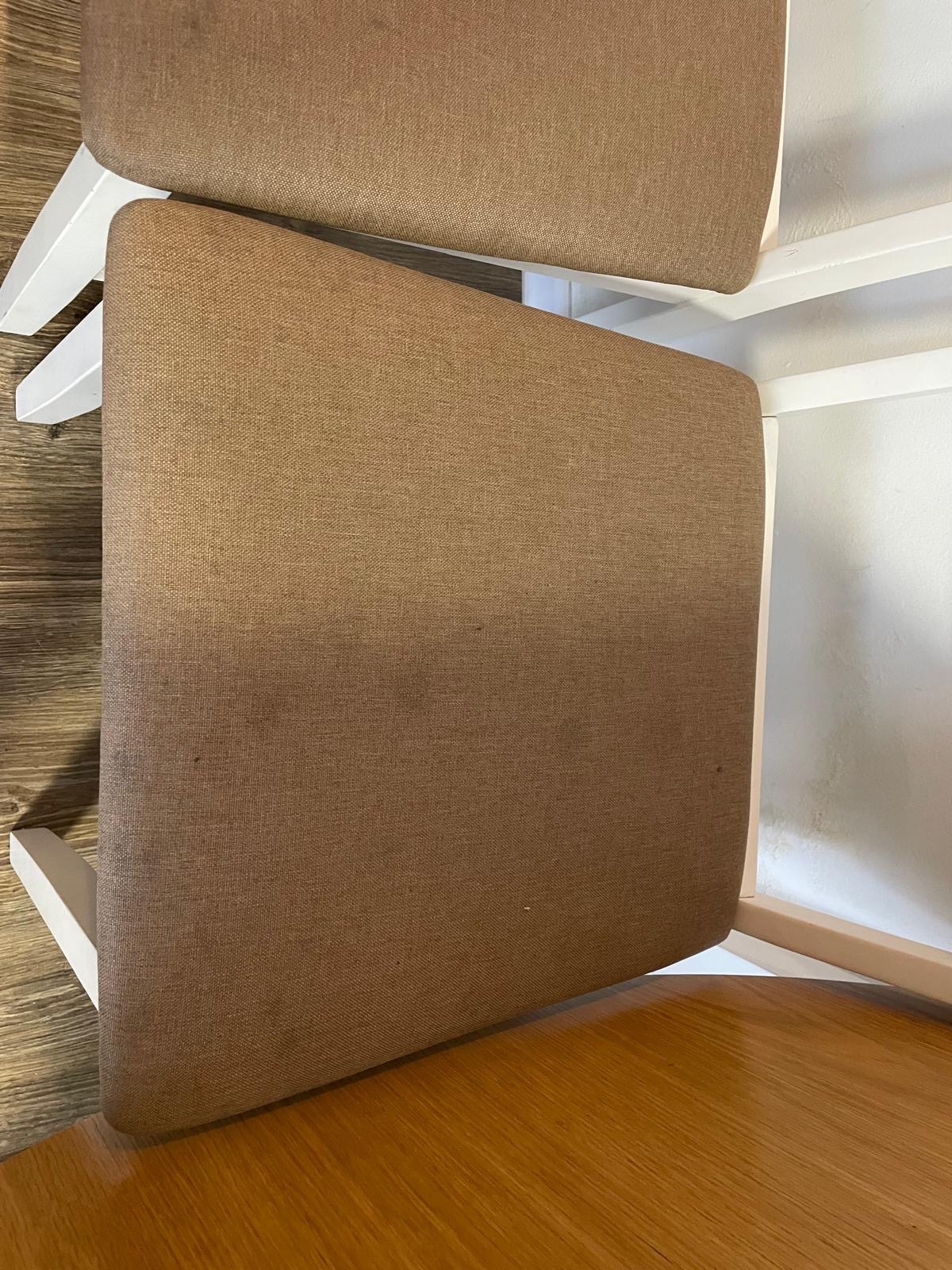 Dwa krzesła z brązową tapicerką i białymi nogami, widoczne z góry, z drobnymi plamkami na tkaninie siedziska.