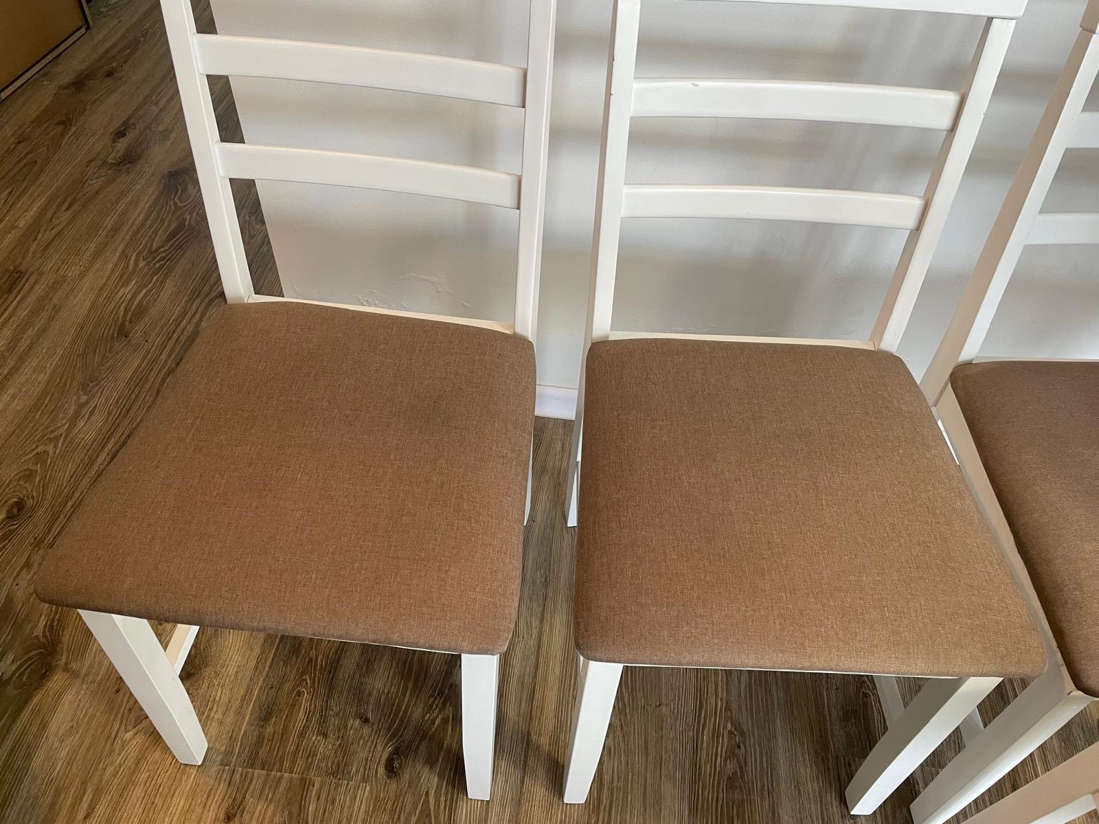 Dwa białe krzesła z brązowymi, tekstylnymi siedziskami, ustawione na drewnianej podłodze, widoczne z bliska.