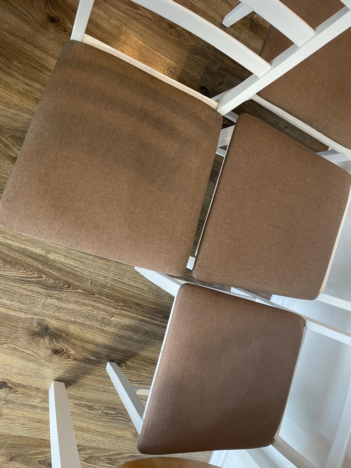 Widok z góry na krzesła z brązowymi tapicerowanymi siedziskami i białymi ramami, ustawione na drewnianej podłodze.