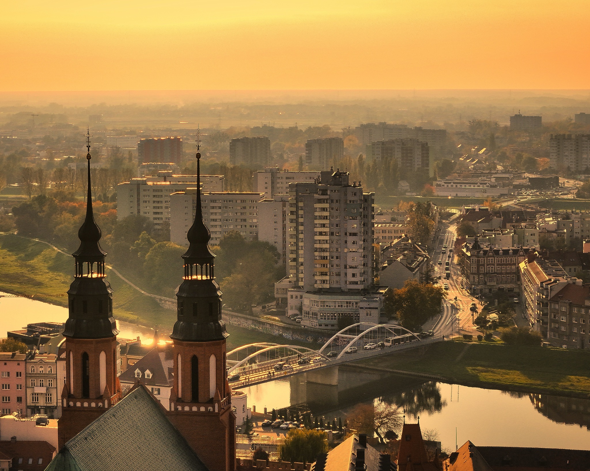 Panorama miasta o wschodzie słońca, z widokiem na rzekę, most i charakterystyczne wieże katedry, spowita delikatną mgłą.