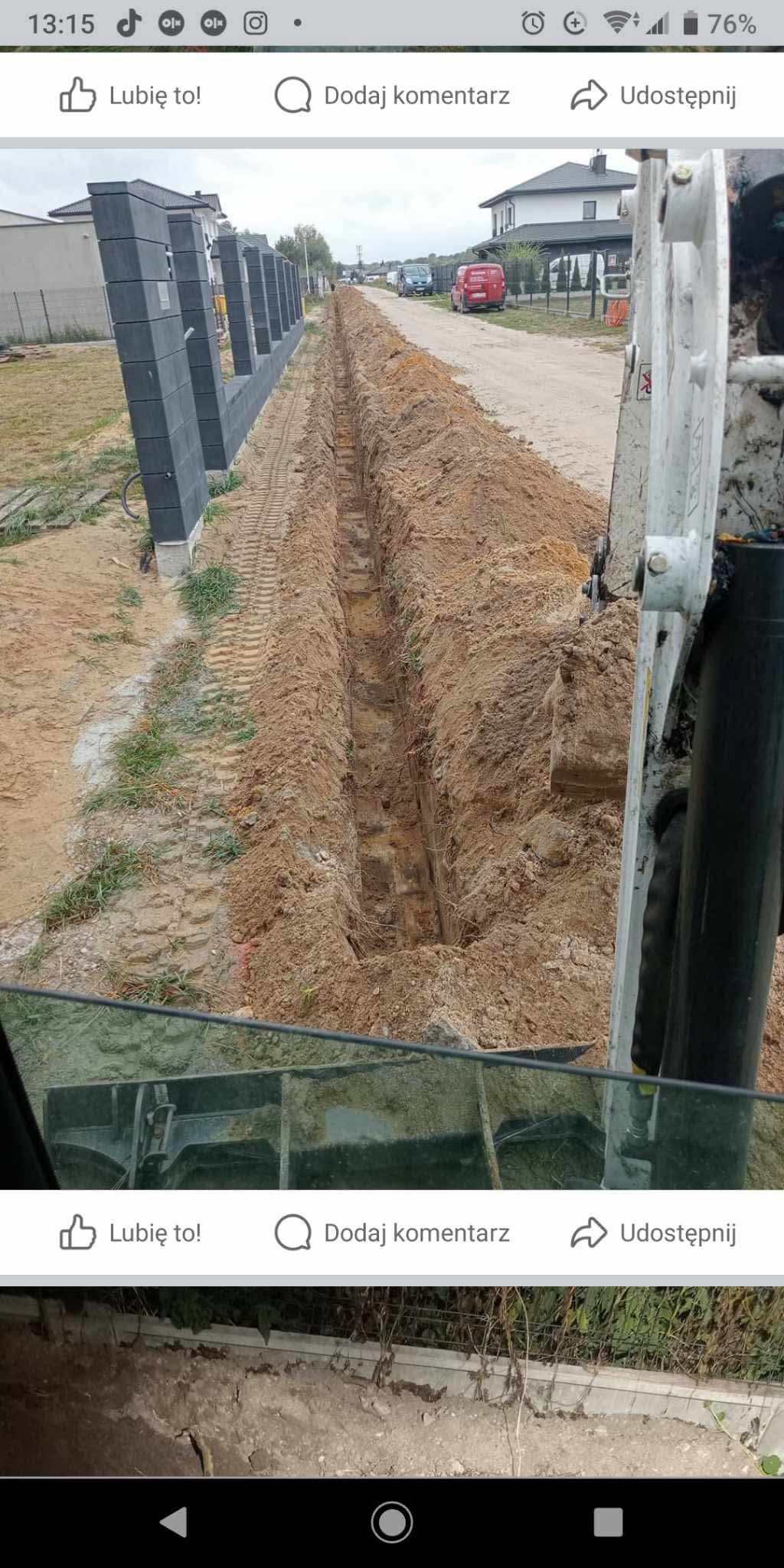Wąski wykop liniowy w ziemi, widok z kabiny maszyny budowlanej, obok betonowe słupki ogrodzeniowe, w tle zabudowa jednorodzinna.