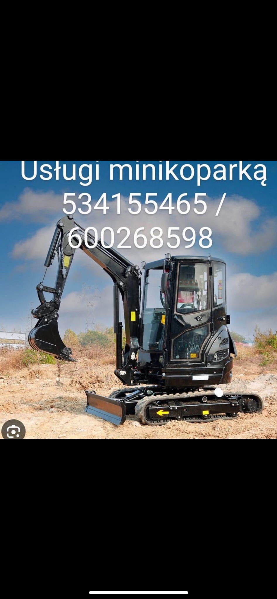 Czarny minikoparka na piaszczystym terenie, z wysięgnikiem skierowanym ku górze, na tle błękitnego nieba z chmurami. Reklama z numerami telefonów widoczna u góry.