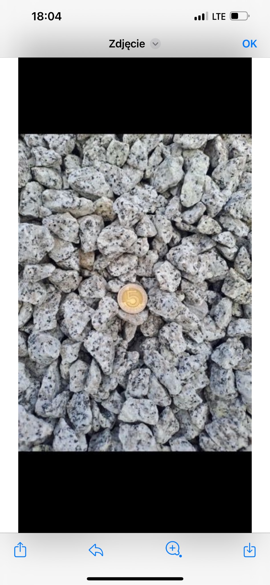 Zbliżenie na biało-szary grys granitowy o frakcji 8-16 mm, z monetą 5 zł dla porównania wielkości.